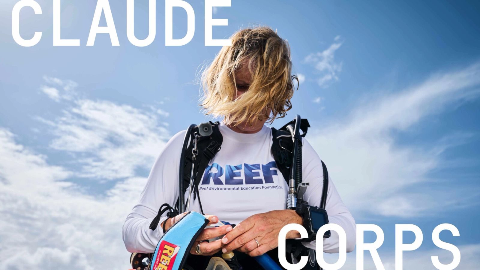 Дайвер в белой рубашке REEF регулирует снаряжение на фоне яркого голубого неба. Источник: Anthropic